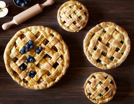 Close up. Homemade pastry apple pie pies bakery on dark wooden kitchen table with raisins, blueberry and apples. Traditional dessert on Independence Day. Flat lay food background.