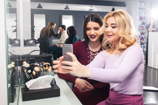 Two beautiful girlfriends are sitting and making selfie in a beauty salon