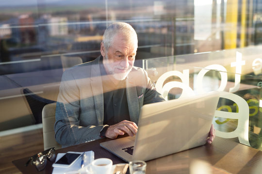 Senior businessman with smartphone and laptop in cafe
