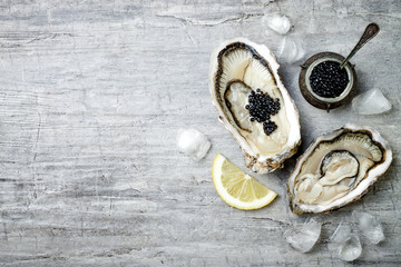Opened oysters with black sturgeon caviar and lemon on ice on grey concrete background. Top view,...