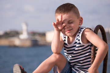 Cool little boy closed his eyes from the sun with his hand in the hot summer