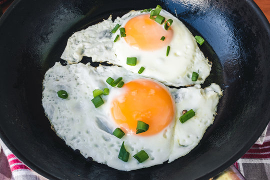Fried eggs with green onion in black pan, close up view