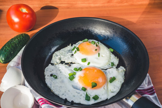 Fried eggs in pan, cucumber and tomato on wooden background