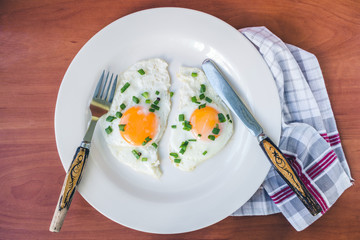 Fried eggs in white plate on napkin at wooden background, top view