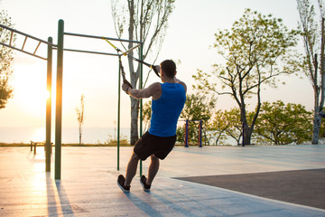 workout with suspension straps In the outdoor gym, strong man training early in morning on the...