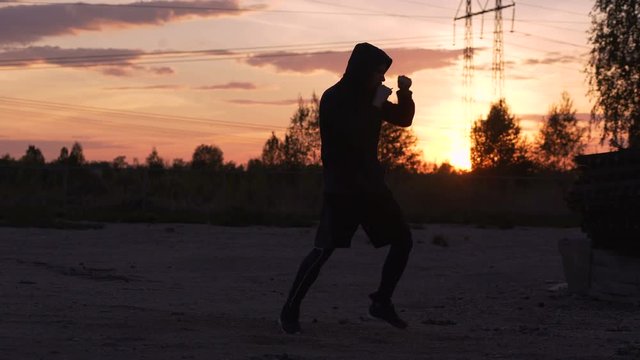 Silhouette of young man boxer training for kicking on sunset at city park