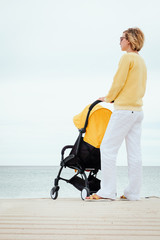 Mother looking through the sea wearing sunglasses while walking alone with baby in stroller
