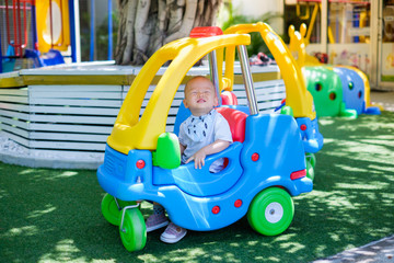 Fototapeta na wymiar Cute little Asian 1 year old toddler baby boy child riding on a colorful small toy car at play ground in the day time, Thailand, Kid first experience concept