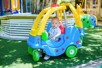 Cute little Asian 1 year old toddler baby boy child riding on a colorful small toy car at play ground in the day time, Thailand, Kid first experience concept