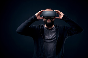 Young hipster bearded man wearing virtual reality goggles. Black background studio VR concept