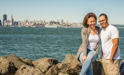 Fototapeta premium Brother and sister sitting on rocks at Treasure Island with San Francisco in background view