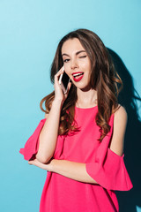 Fototapeta premium Pretty girl in dress winking while talking on mobile phone