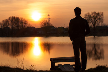 Fototapeta premium Man silhouette, standing on river stones gangway and contemplating a beautiful sunset.