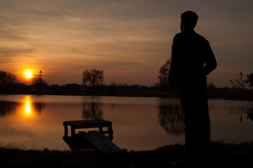 Man silhouette, standing on river stones gangway and contemplating a beautiful sunset.