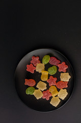 Colorful jelly candies on a black plate background.