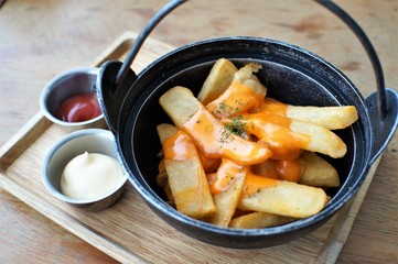 A bowl of french fries topping with melting cheese on wooden plate