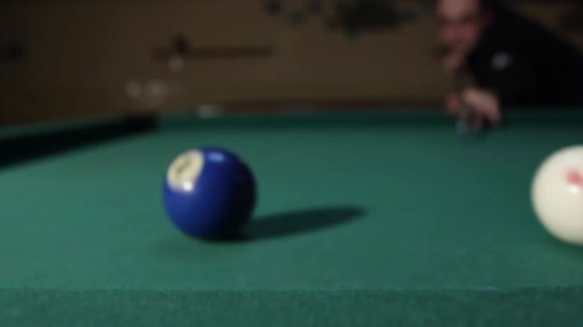 Player performs billiard trick shot from the table edge, he throws blue ball in the hole. American billiard, 9-ball, nine-ball pool.