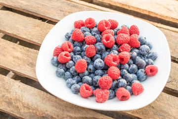 Himbeeren und Blaubeeren auf einem weißen Teller vor Holz Hintergrund
