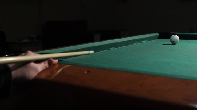 Billiard player with stick and white ball throws pink ball in the hole, close up. Billiard game in dark pub. American billiard, 9-ball, nine-ball pool.