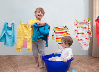 little mother's helpers kids happy brother and sister  in the laundry to wash clothes, playing. Baby clothes hanging on the clothesline.
