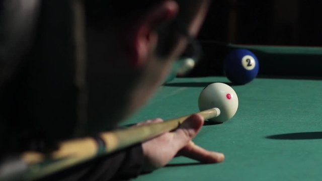 Guy playing pool in pub. Billiard player taking a shot, hitting the cue ball and she hit blue ball No 2. Blue ball into the hole. American billiard, 9-ball, nine-ball pool.