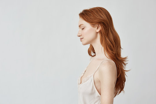 Portrait of redhead girl in profile with closed eyes smiling.