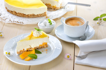 Kuchen ohne Backen: Mango-Frischkäsekuchen mit Boden aus Kekskrümeln, dazu eine Tasse Kaffee mit Crema  - Mango cheesecake  from the refrigerator without baking, served with a cup of coffee