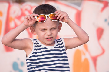adorable small boy with sunglasses and sailor shirt on graffiti wall background