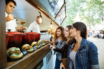 Three beautiful young women buying meatballs on a food truck.
