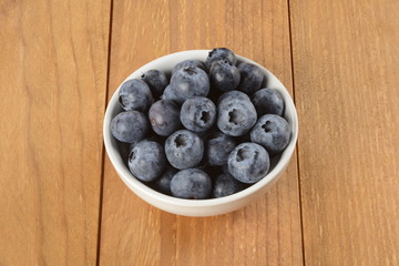 Arándanos en un bol blanco sobre mesa de madera marrón