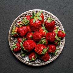 fresh ripe useful fruit strawberry in a clay bowl closeup on a black background