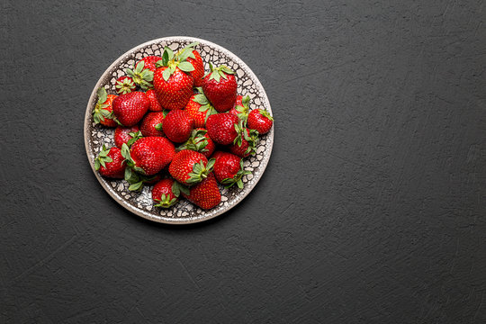 fresh ripe useful fruit strawberry in a clay bowl closeup on a black background