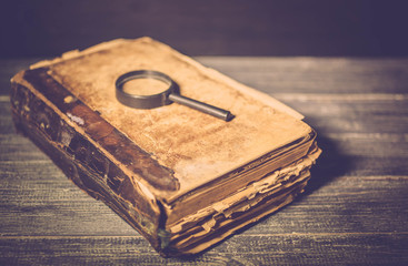Old brown book and magnifying glass on tree background. Close up. Vintage toning. Selective focus.
