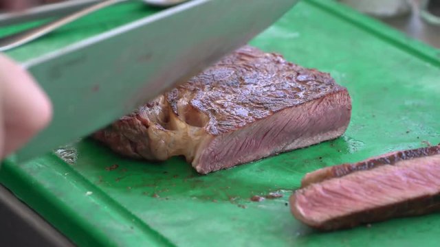 Man cut steak with a sharp knife on green plastic cutting board.