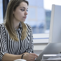 Giovane segretaria con camicia a righe e cuffie è seduta alla sua scrivania nel suo ufficio