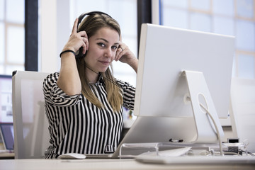 Giovane operatrice di call center con camicia a righe e cuffie è seduta alla sua scrivania nel suo...