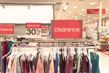Red clearance sign for 30% off on cloth rack with variety of women apparel in retail store in...