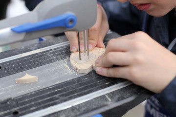 Small boy hands working with fret to saw board. Classes for young carpenter cutting wood form using...