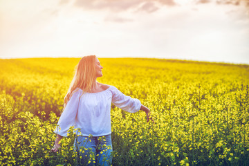 Fototapeta premium Smiling woman walking in yellow rapeseed field at sunset
