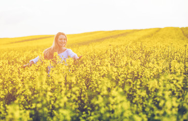Fototapeta premium Smiling woman walking in yellow rapeseed field at sunset