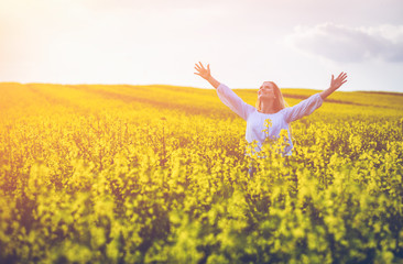Naklejka na ściany i meble Smiling woman walking in yellow rapeseed field at sunset