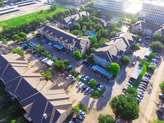 Aerial view of typical multi-level apartment building complex with swimming pool, surrounded by green garden and rows of cars in parking lots in Houston, Texas, US. Residential recreation concept.