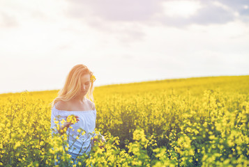 Fototapeta na wymiar Smiling woman in yellow rapeseed field at sunny day