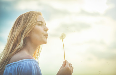 Beautiful girl blowing dandelion on sky