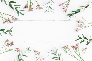 Fototapeta na wymiar Flowers composition. Frame made of eucalyptus leaves and pink flowers on white wooden background. Flat lay, top view
