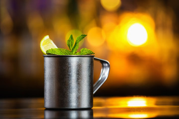 Closeup mug of moscow mule cocktail decorated with mint and lemon at bar counter background.