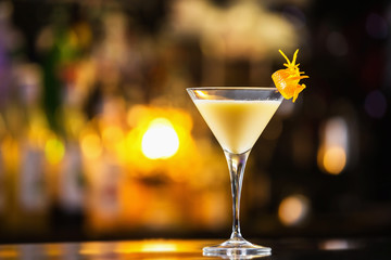 Closeup glass of eggnog cocktail decorated with orange at bright bar counter background.