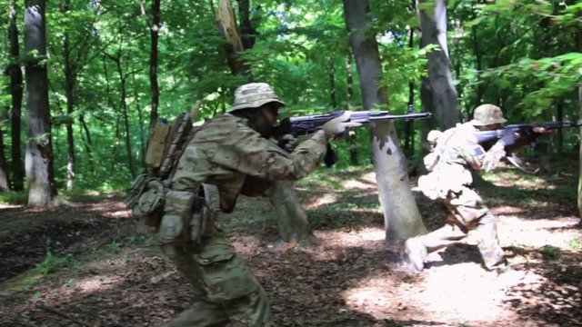 Guerilla partisan warriors attacking aiming in forest ambush carrying their guns. War battlefield maneuvers training. Steadicam shot.