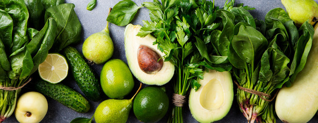 Green vegetables and herbs assortment on a grey stone background. Top view.