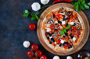 Hot testy pizza with tomatoes, mozzarella, mushrooms, olives, red pepper and basil on black concrete background. Copyspace. Top view.